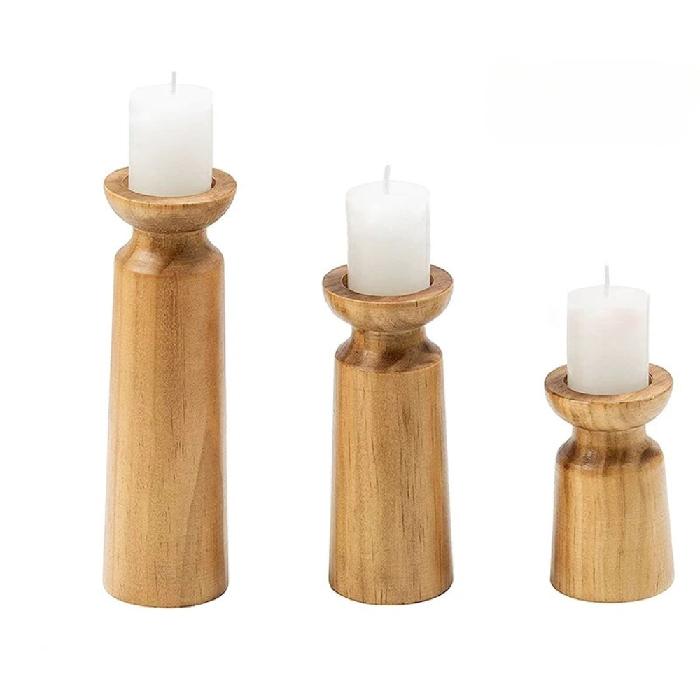 Three carved pine candle holders of varying heights with white pillar candles.