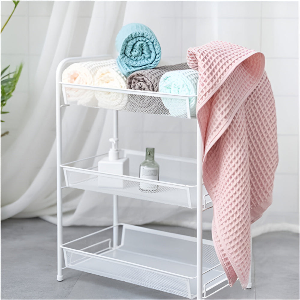 A white metal shelf unit holding rolled towels and toiletries, with a pink waffle-weave towel draped over the side.