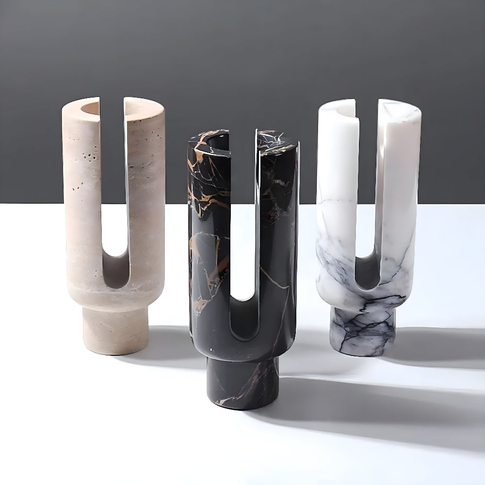 Three sculptural candle holders in beige, black marble, and white marble.