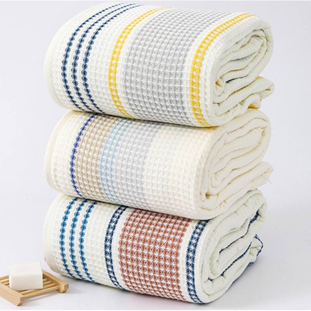 Three stacked cotton bath towels with honeycomb weave and colorblock stripes in blue, yellow, and brown.