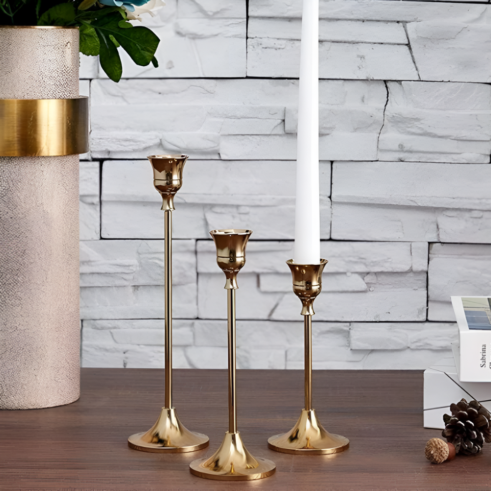 Three gold taper candle holders of varying heights on a wooden surface.