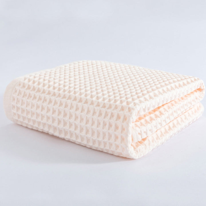 A folded light peach cotton waffle weave bath towel.