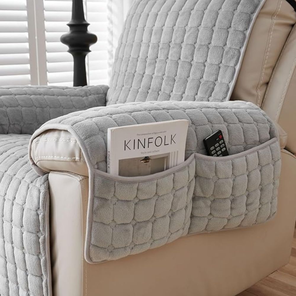 Gray quilted recliner chair armrest cover with side pockets holding a magazine and remote.