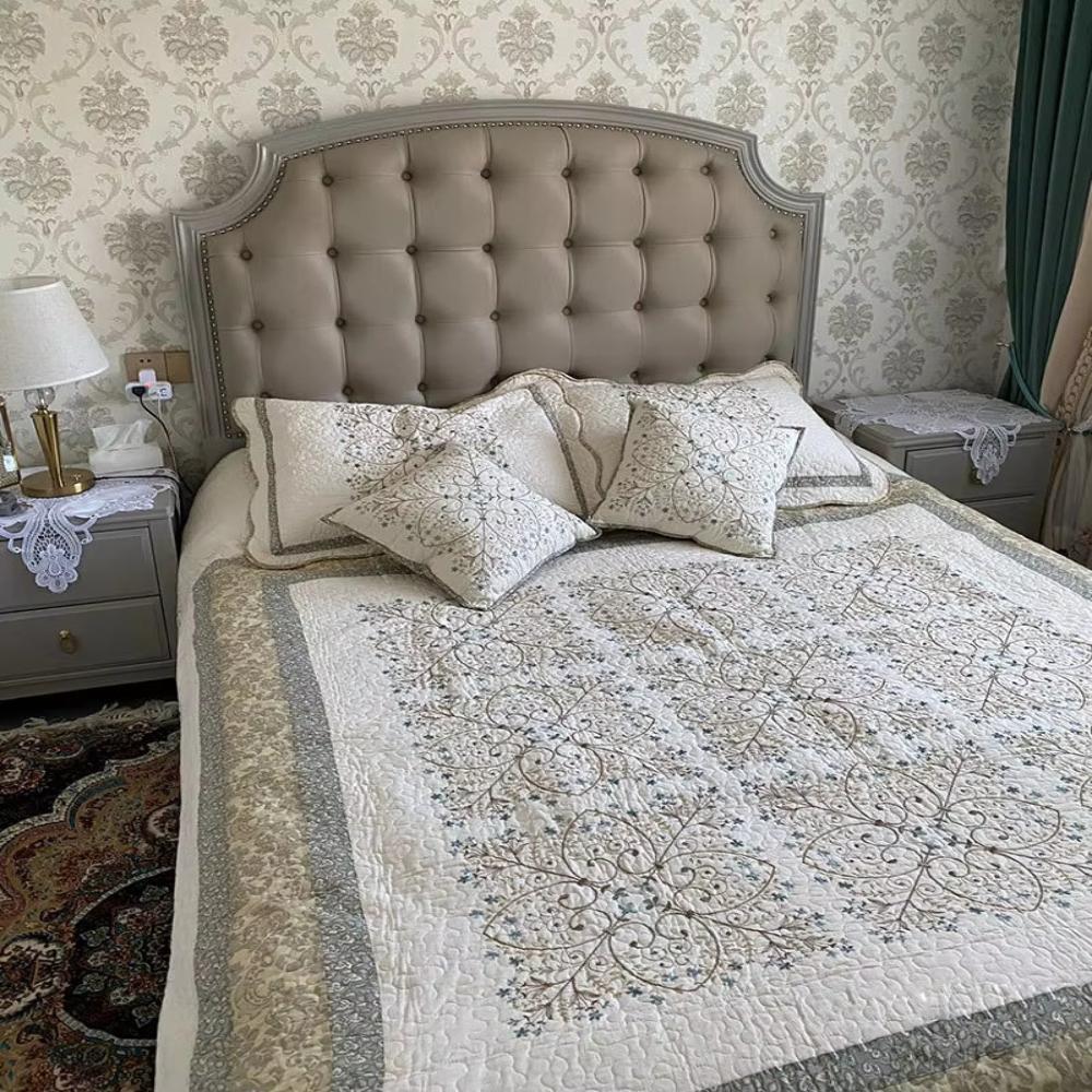 Elegant embroidered patchwork thread coverlet on a bed with tufted headboard and nightstands.