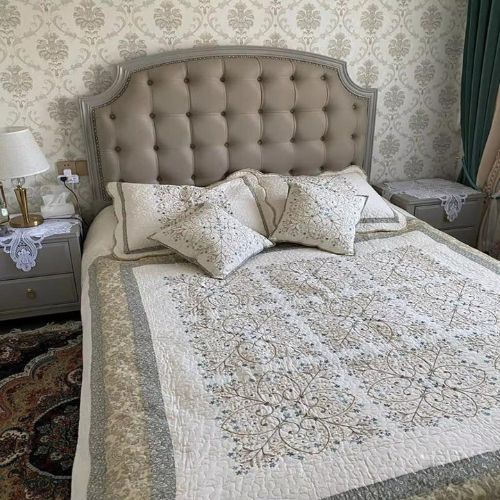Elegant embroidered patchwork thread coverlet on a bed with tufted headboard and nightstands.