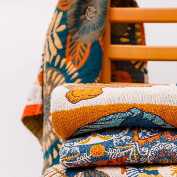 Stack of folded reversible cotton beach towels with vibrant floral and bird patterns in blue, orange, and yellow.