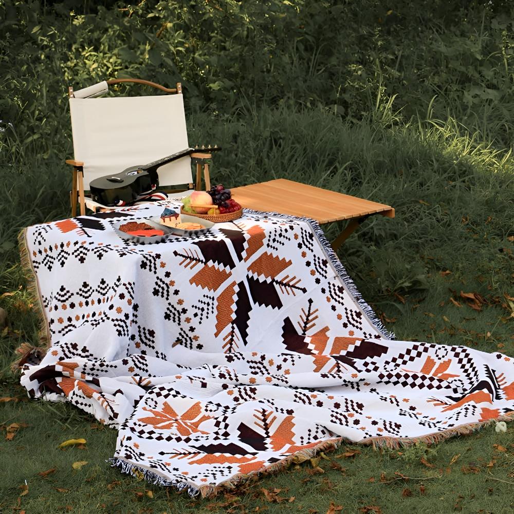 Moroccan Boho picnic mat with geometric patterns spread on grass with a chair, table, and fruit.