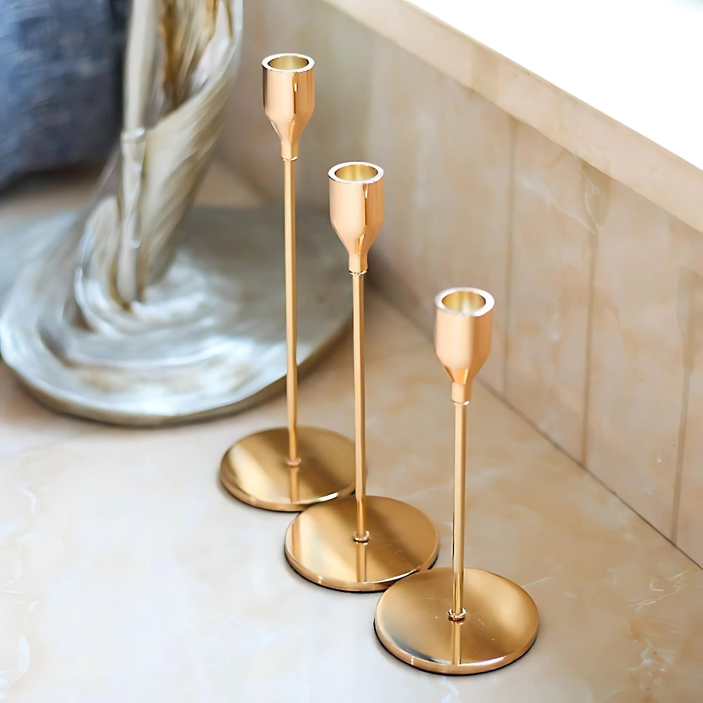 Three tall gold stainless steel candle holders in varying heights on a marble surface.