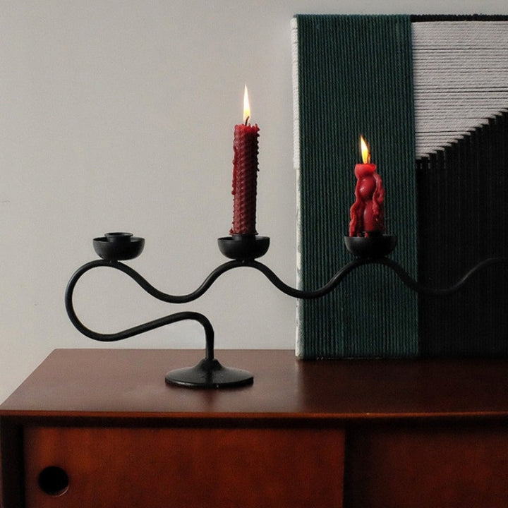 Black iron tri iron twisted candle holder with two red candles lit.