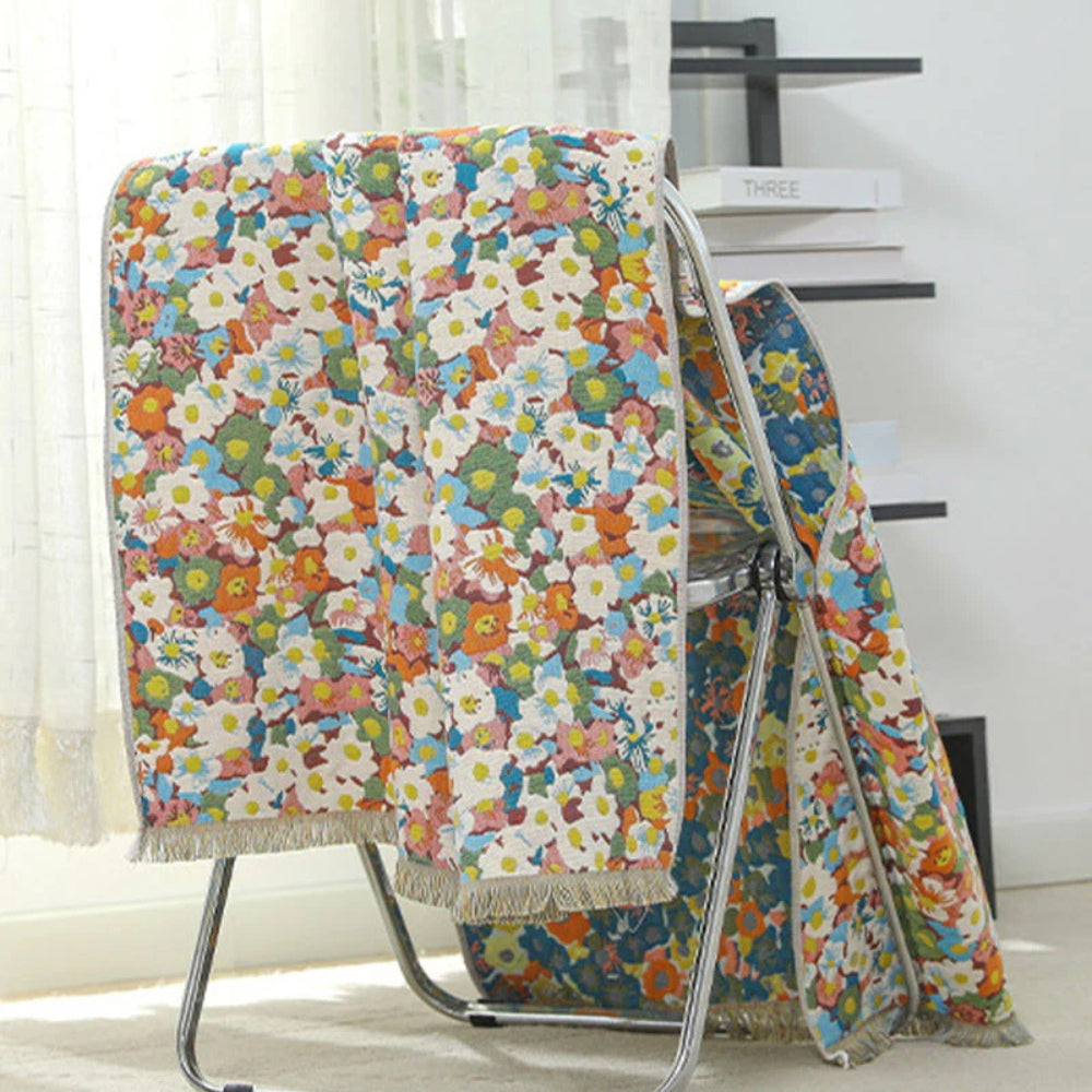 Reversible cotton bath towel with a colorful floral print and fringed edges, draped over a metal rack.