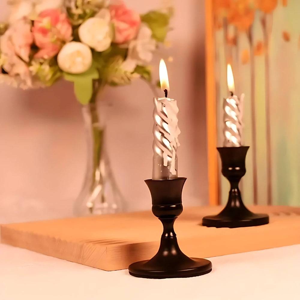 Two black vintage taper candle holders with shimmering silver candles lit.