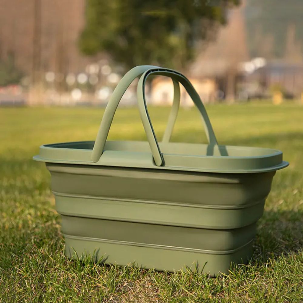 Green collapsible storage basket with handles sitting on grass.