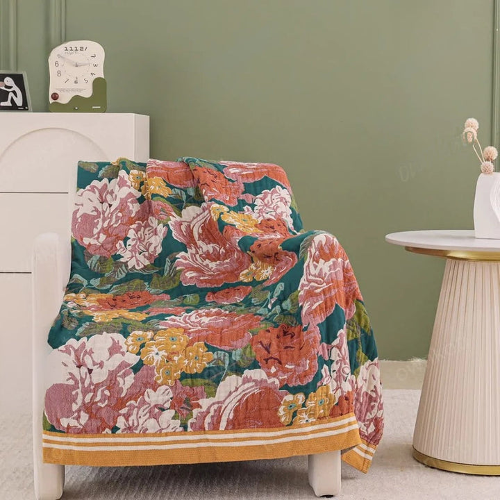 A white armchair draped with a colorful floral cotton blanket featuring large pink, orange, and yellow flowers on a teal background.