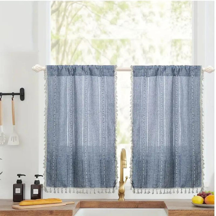 Blue boho kitchen curtains with white jacquard stripes and tassels, hanging on a window.