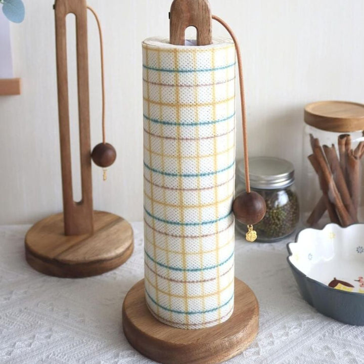 Acacia wood paper roll stand with a plaid paper towel roll and a wooden ball stopper.