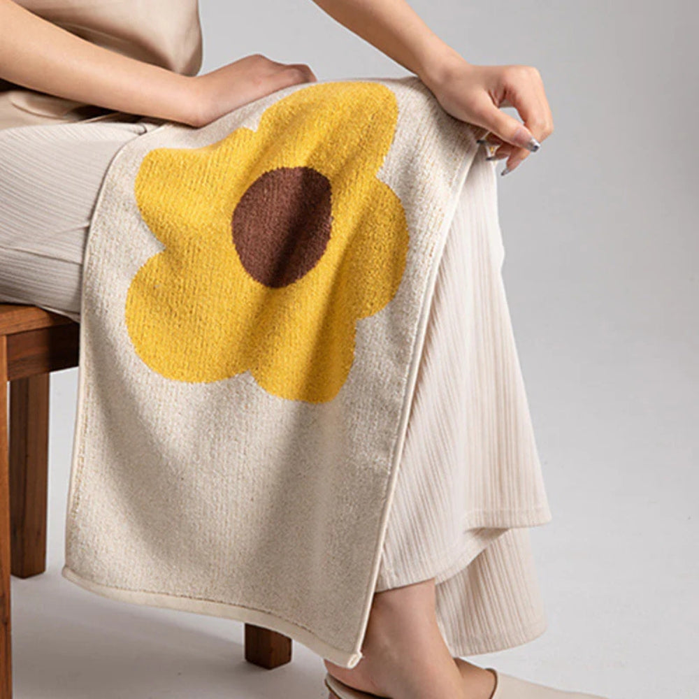 A person sitting with a beige cotton bath towel featuring a large yellow sunflower print draped over their lap.