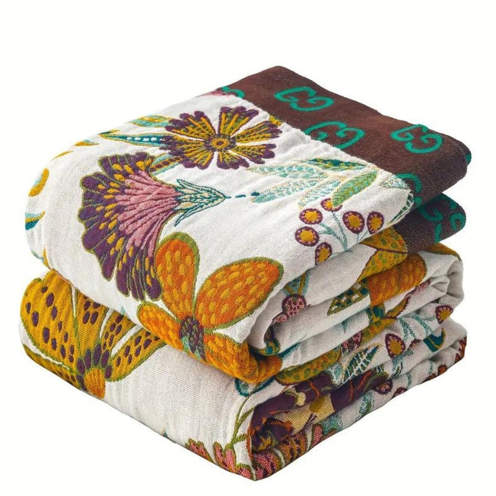 Stack of three folded cotton throws with a floral pattern and brown trim with green GG logo.
