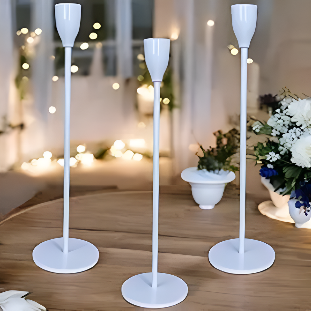 Set of three white metal taper candle holders of varying heights on a wooden table.