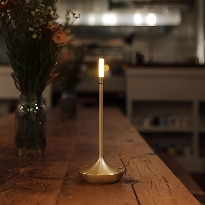 Portable aluminum table lamp with a candle-style light and a loop handle on a wooden table.