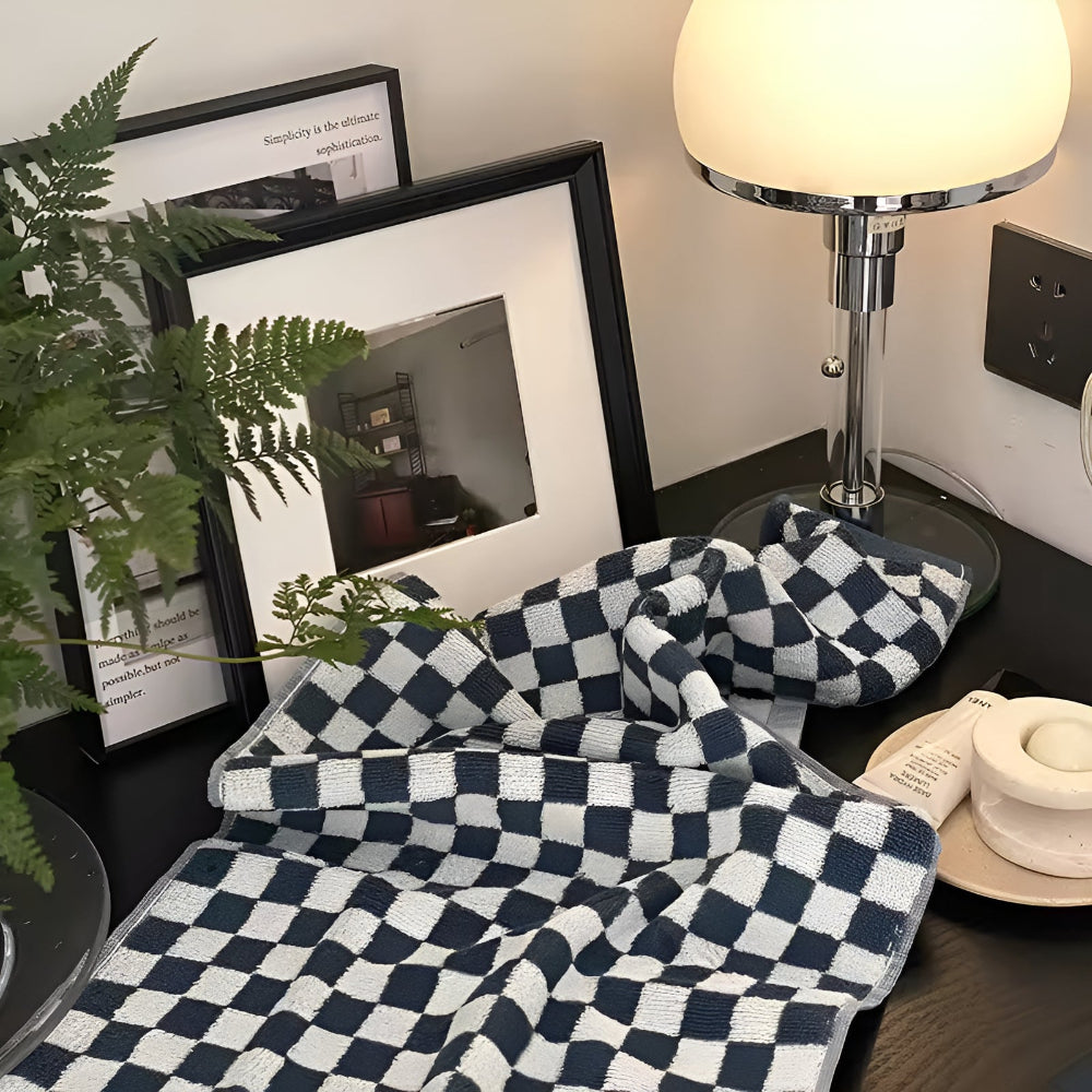 Blue and white checkered cotton towel draped on a black surface next to framed pictures and a lamp.