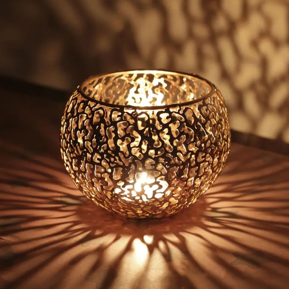 A round, metallic tealight holder with a geometric cutout pattern, casting intricate shadows.