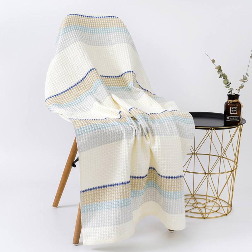 A waffle-weave cotton bath towel with horizontal stripes in cream, blue, and tan draped over a chair.