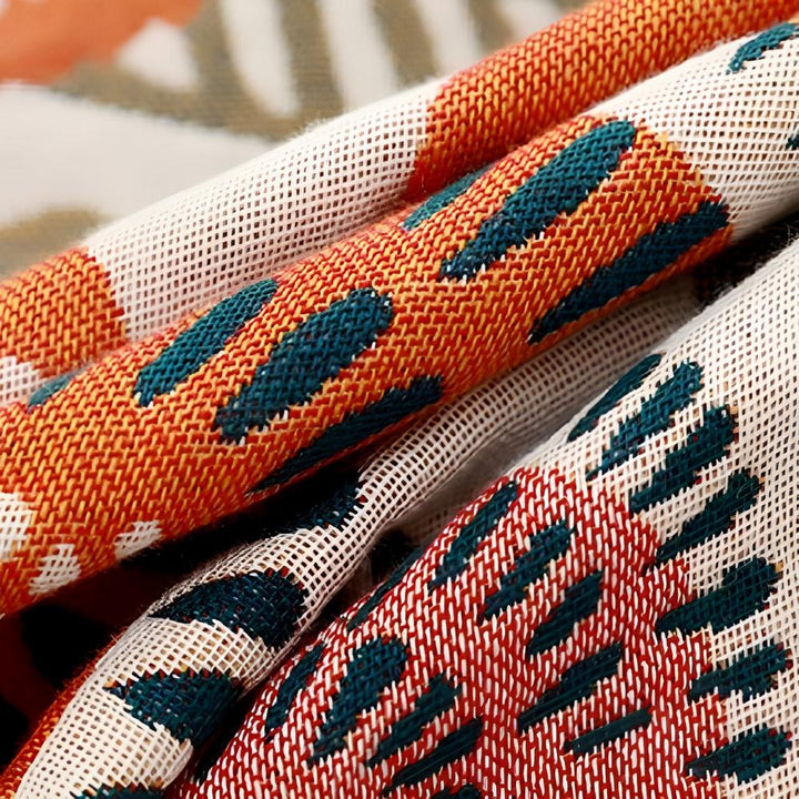Close-up of a rolled cotton bath towel with a red, orange, and teal abstract pattern.