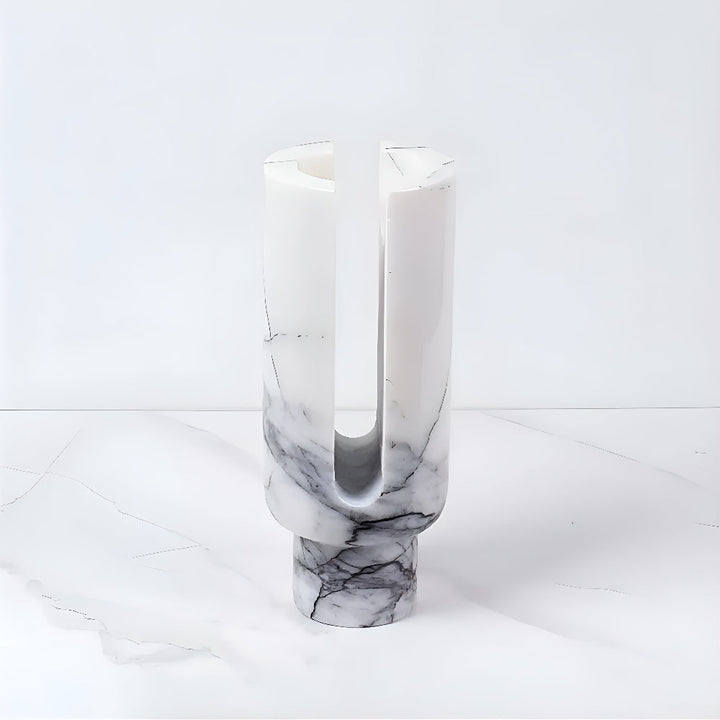 Sculptural marble candle holder with a U-shaped opening and a cylindrical base.