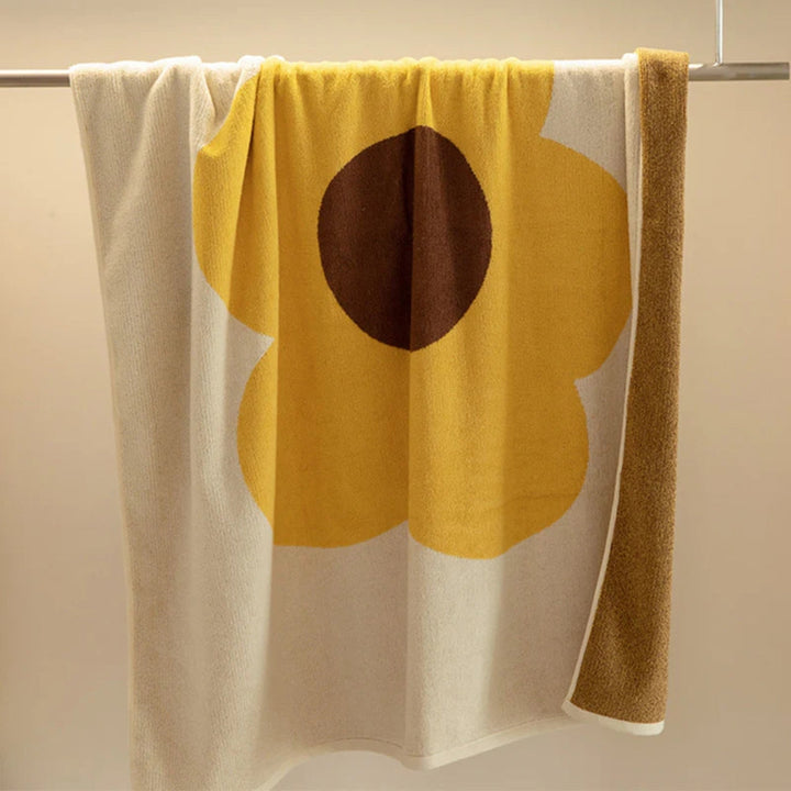 Cream and yellow floral cotton bath towel with a brown center, hanging on a towel rack.