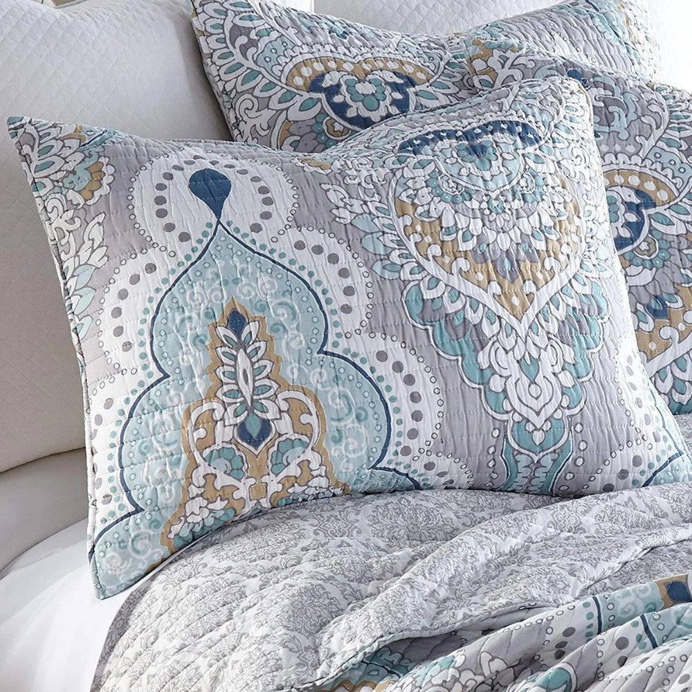 Paisley aqua teal coverlet with decorative pillows on a bed.