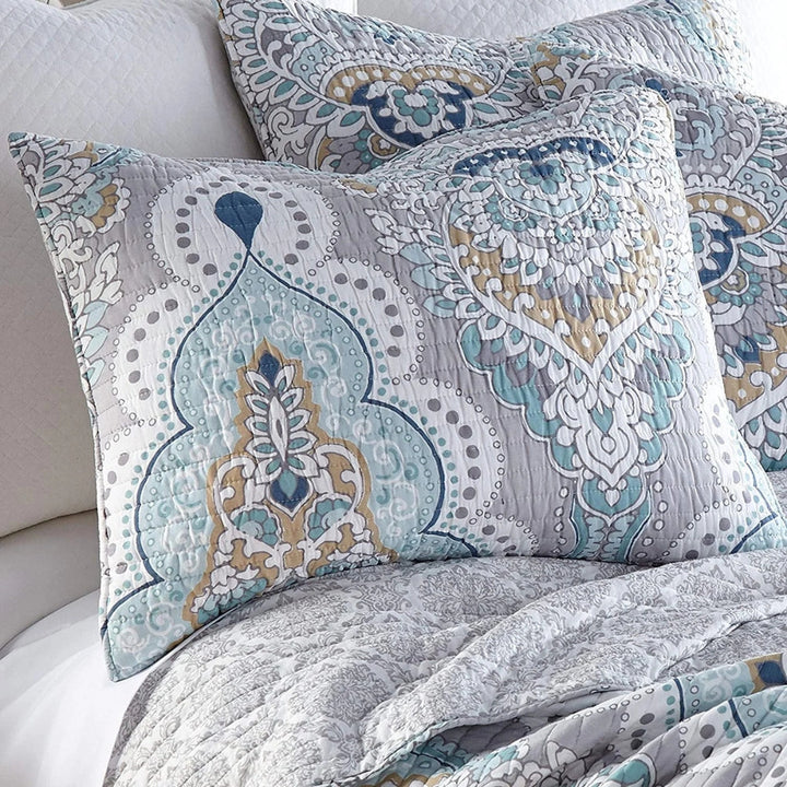 Paisley aqua teal coverlet with decorative pillows on a bed.