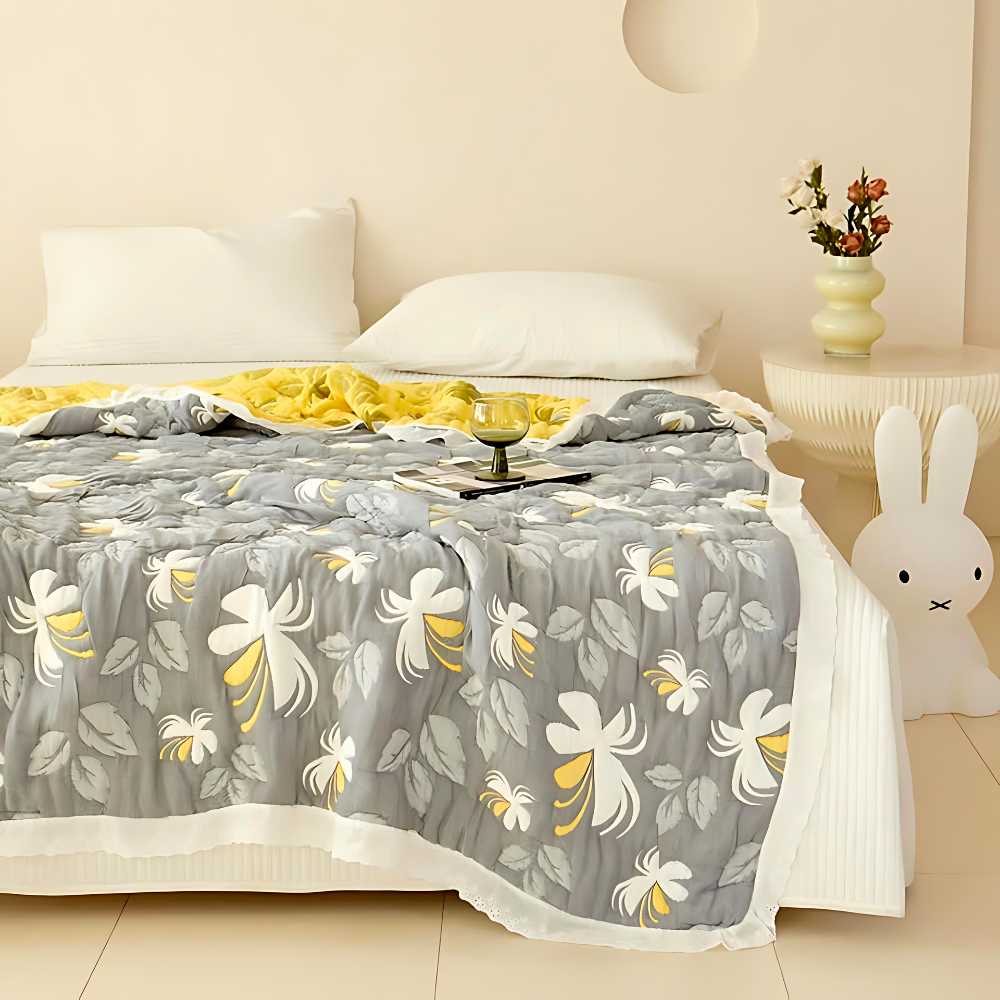 Elegant floral summer blanket in grey with yellow and white flowers, draped on a bed with white pillows.