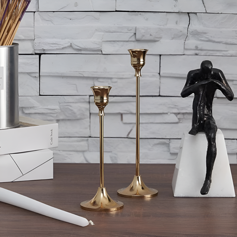Two gold taper candle holders and a black sculpture on a wooden table.