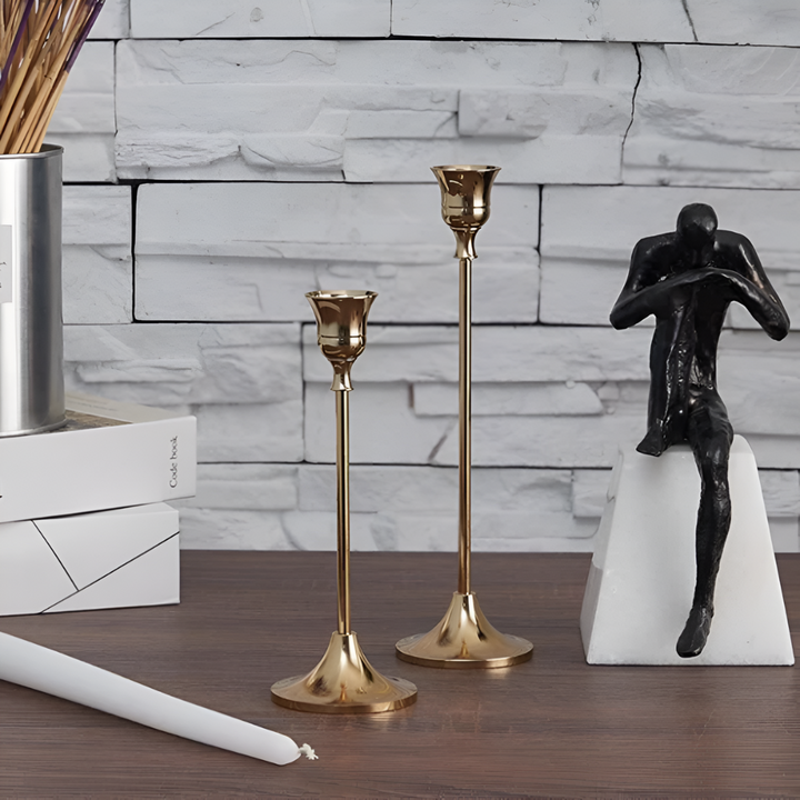 Two gold taper candle holders and a black sculpture on a wooden table.