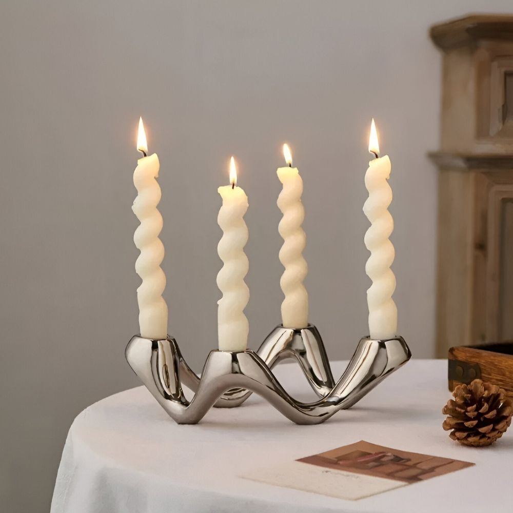 Silver ceramic candle holder with four twisted white candles, on a white tablecloth.