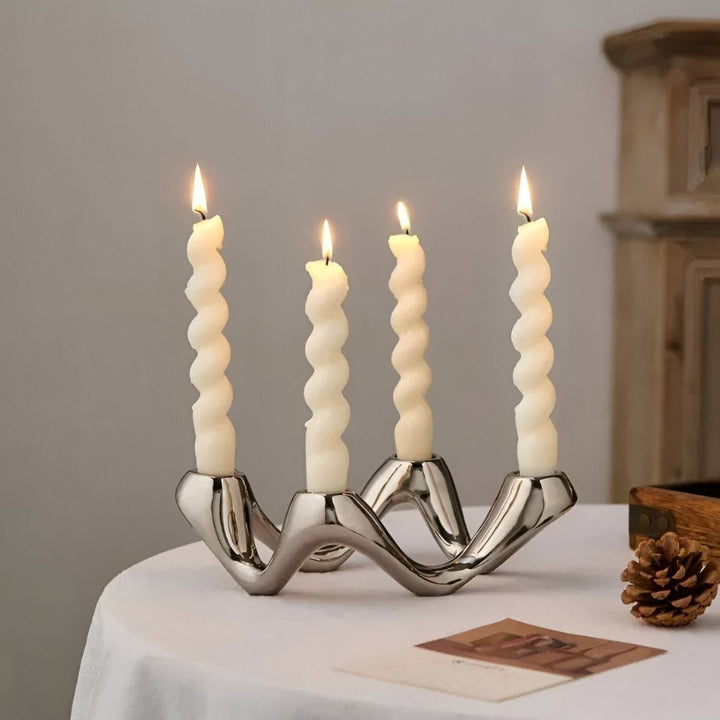 Silver ceramic candle holder with four twisted white candles, on a white tablecloth.