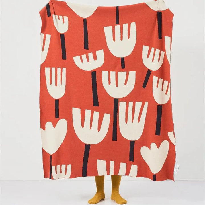 Red knitted blanket with a pattern of cream-colored tulips and black stems.