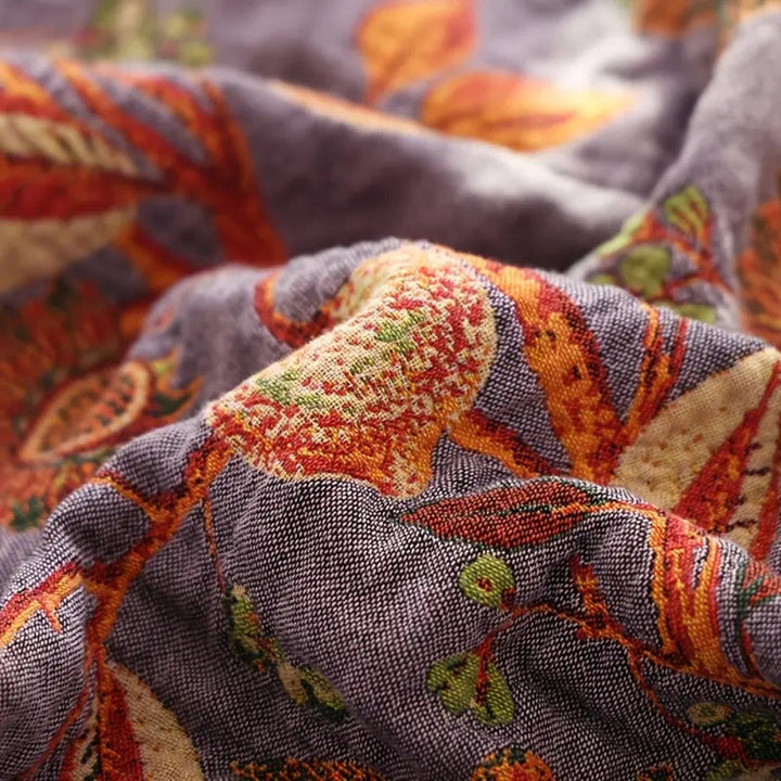 Close-up of a soft, breathable cotton blanket with a botanic floral pattern in shades of purple, orange, and green.