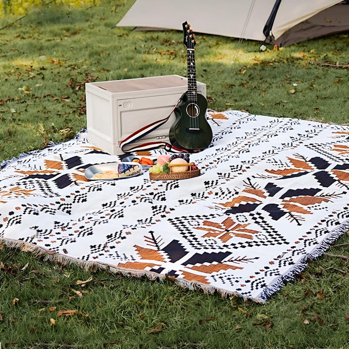 Moroccan Boho picnic mat with a geometric pattern, a ukulele, and food laid out on the grass.