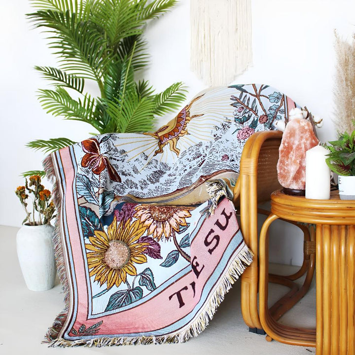Celestial tapestry throw with sun tarot card design and floral border draped over a chair.