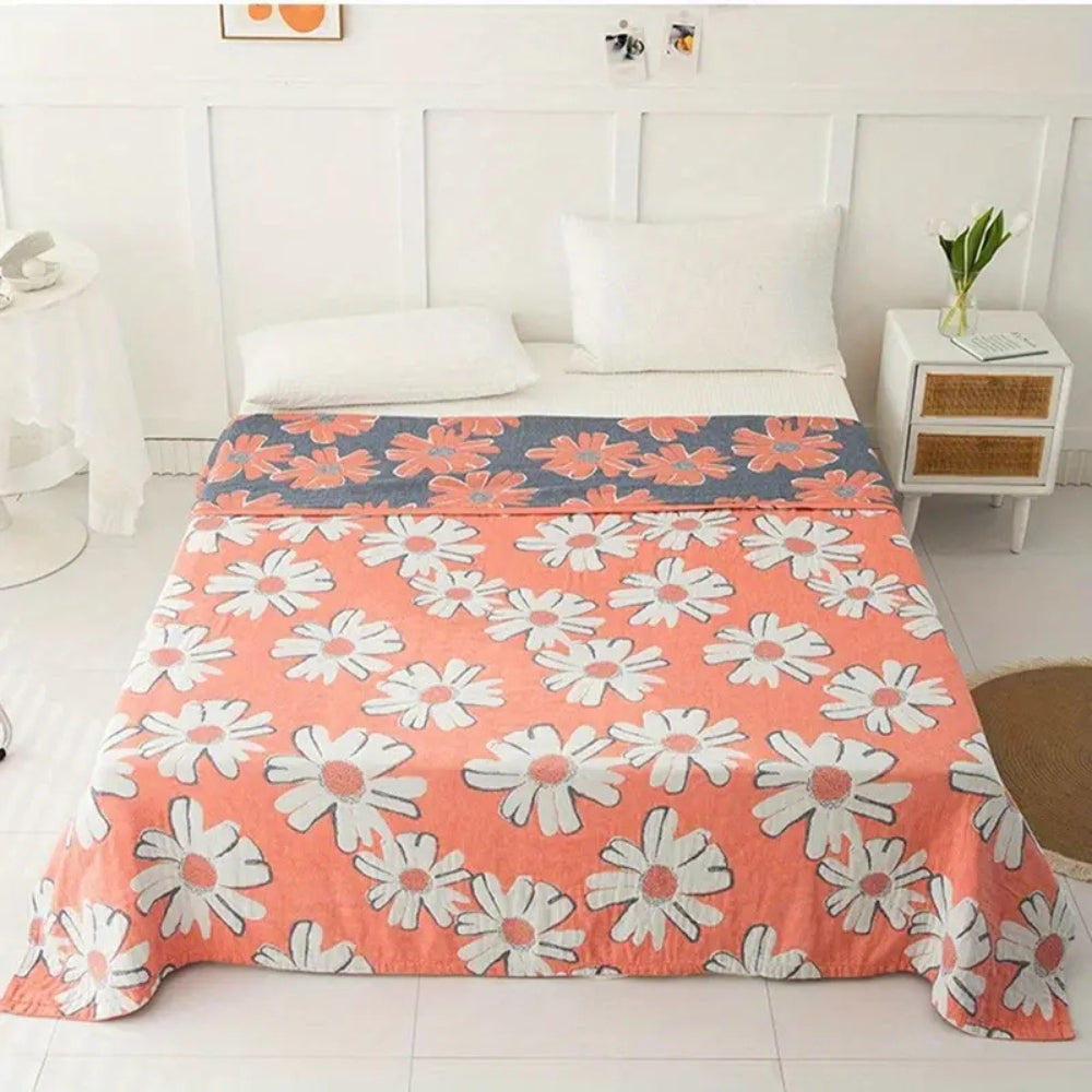 A coral pink cotton blanket with a pattern of white daisies and a grey band with daisy pattern.
