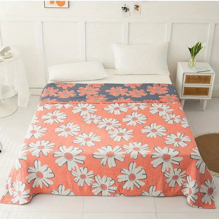 A coral pink cotton blanket with a pattern of white daisies and a grey band with daisy pattern.