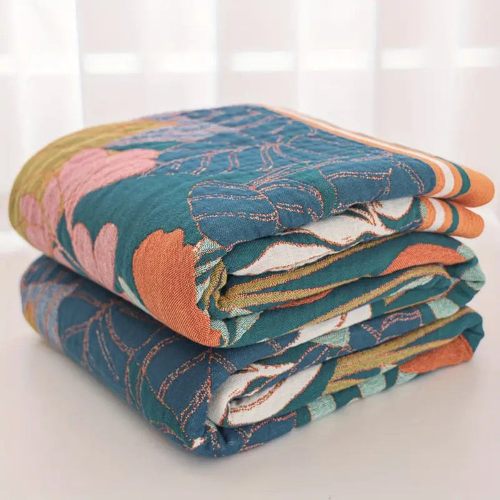 A stack of two folded cotton gauze blankets with a garden-inspired floral and leaf pattern in teal, pink, and orange.