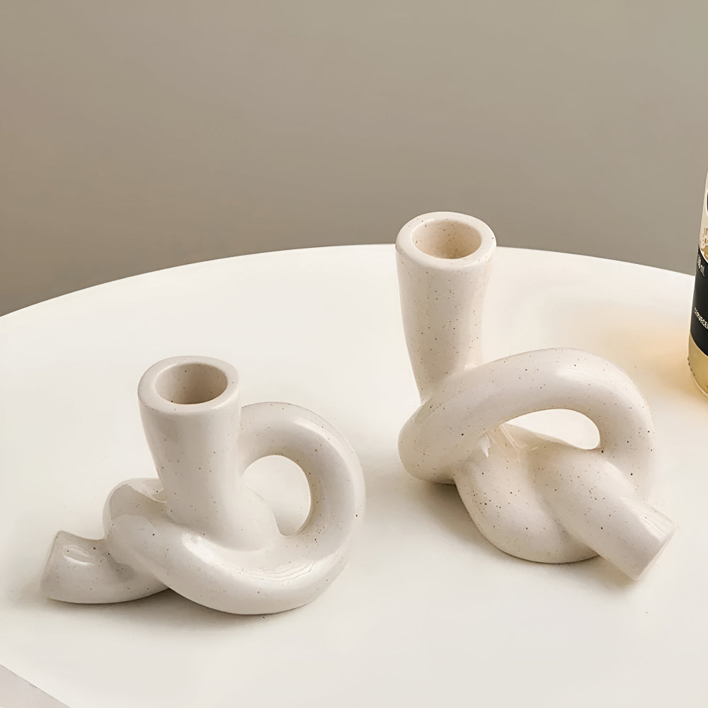 Two white ceramic knot candle holders on a white table.