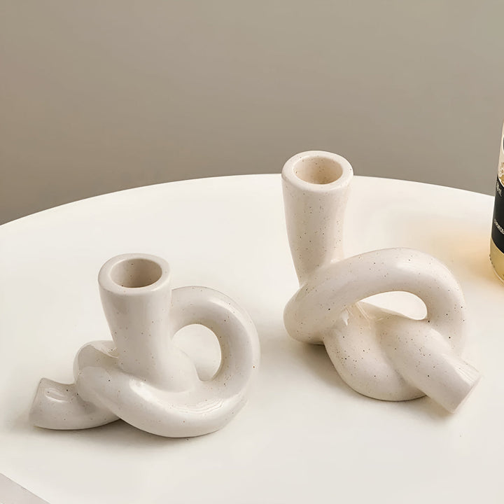 Two white ceramic knot candle holders on a white table.