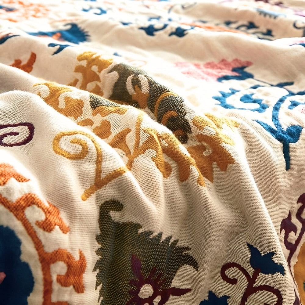 Close-up of a breathable cotton gauze coverlet with embroidered floral and paisley patterns in yellow, blue, orange, and green.