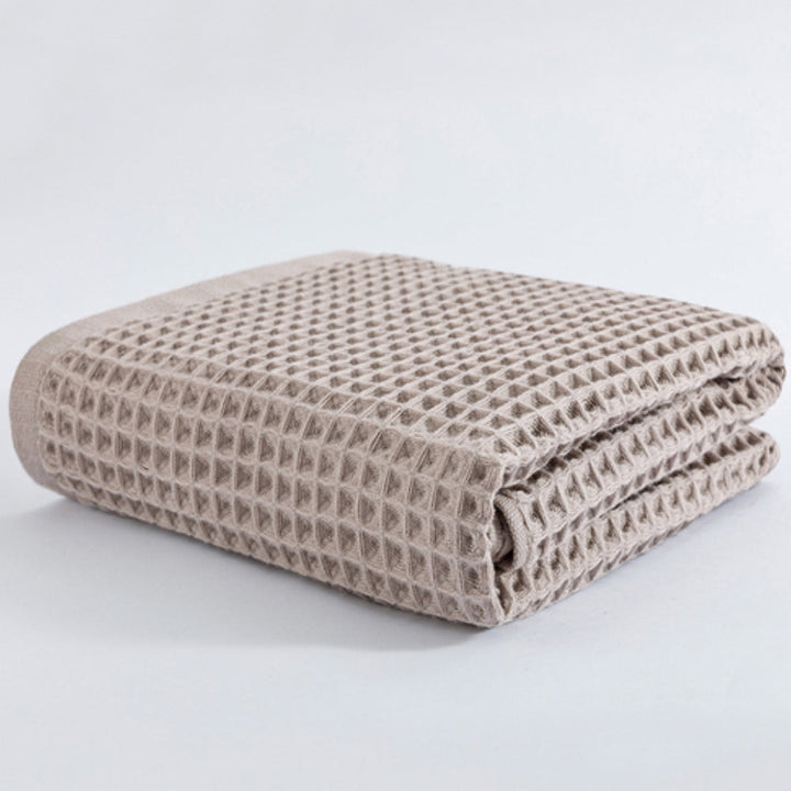 A folded beige cotton waffle bath towel on a white background.