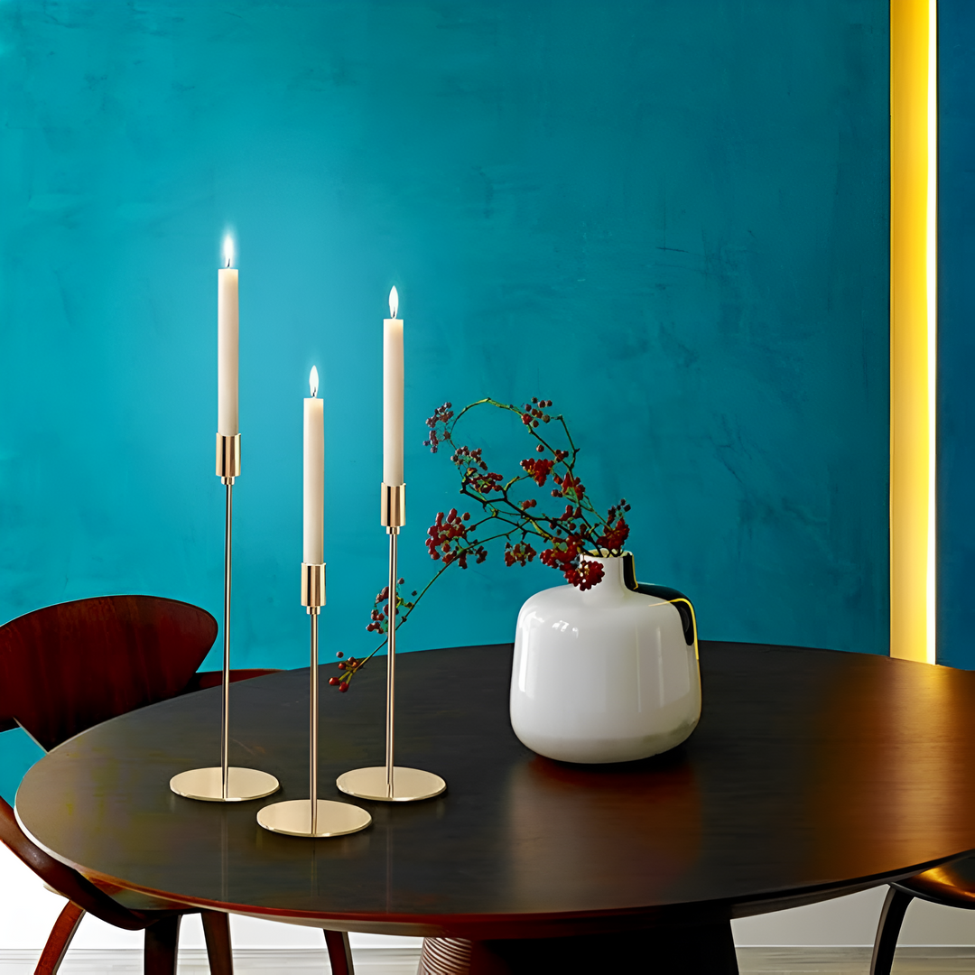 Three brushed metal taper candle holders of varying heights on a dark wooden table.
