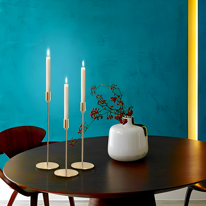 Three brushed metal taper candle holders of varying heights on a dark wooden table.