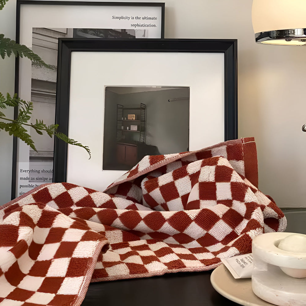 Red and white checkered cotton towel draped over a table with framed pictures in the background.